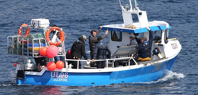 He wrapped himself in a brown knitted sweater with a blue life jacket over it as he filmed scenes aboard a fishing boat with baskets.