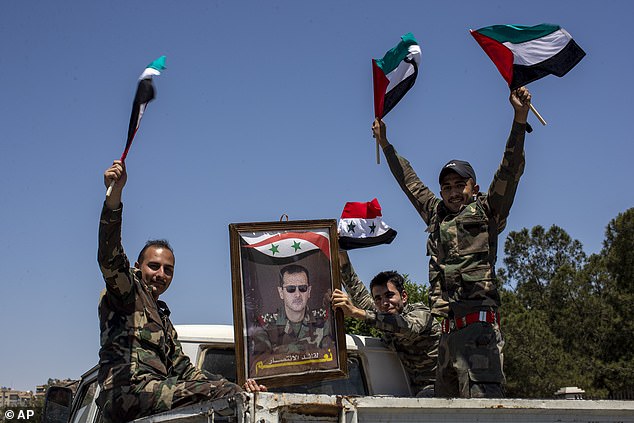 Syrian soldiers hold up Baath Party flags and a portrait of Syrian President Bashar Assad in Arabic reading 