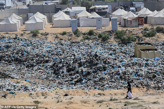 A woman rescues items from a waste dump spreading along a tent camp west of Nuseirat in the Gaza Strip on May 21, 2024