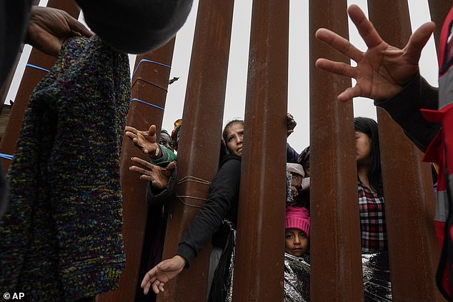 Migrants reach through a border wall for clothing distributed by volunteers as they wait between two border walls to seek asylum in San Diego