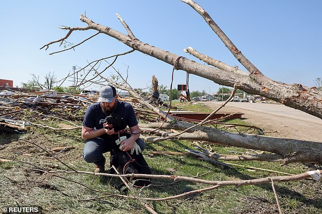 Phillip Ergish of Greenfield, Iowa holds his dog Kobe as he looks at the remains of his home