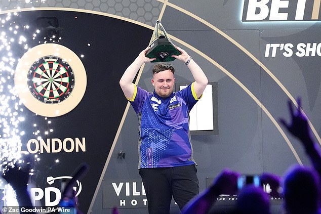 The 17-year-old raises the Premier League Darts trophy above his head in celebration