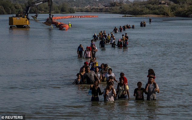A caravan wades past a series of buoys built to deter migrants crossing the Rio Grande River as they search for an opening in the ripcord to enter the US.