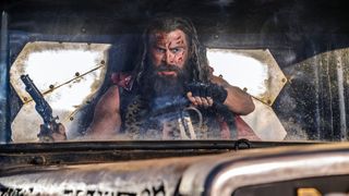 Dementus drives angrily in his car with his gun in his right hand in Furiosa: A Mad Max Saga