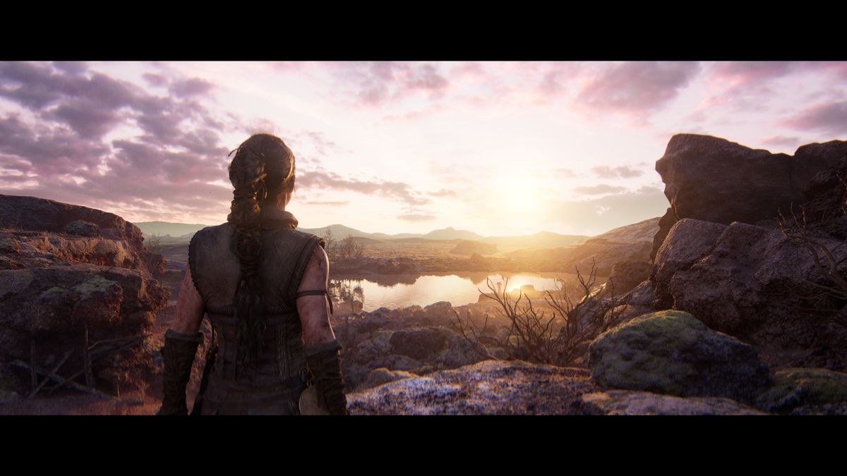 Senua from Hellblade 2 stands watching a beautiful sunrise over a rugged landscape