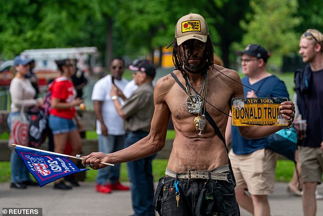 Outside the rally, a shirtless Trump supporter walks around wearing jeans, a flag and a Trump license plate