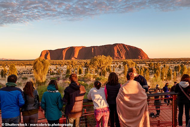 Tourists, including some from China, watch the sun rise at Uluru