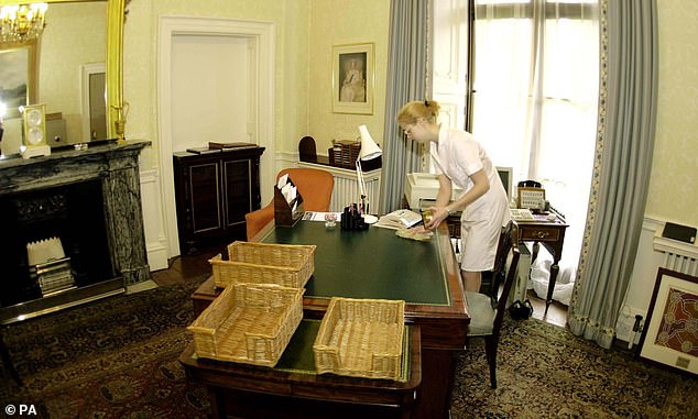 A cleaner hard at work before staff arrive at one of the many desks in a Buckingham Palace office, 2000