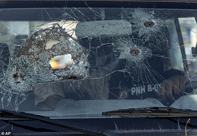 A police officer sits in his vehicle with a windshield damaged by bullet holes, in Port-au-Prince, Haiti, Saturday, May 11, 2024