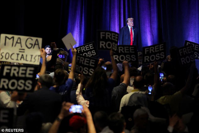 A homemade 'MAGA + Socialist' sign is held by an attendee at this weekend's Libertarian National Convention as former President Donald Trump speaks