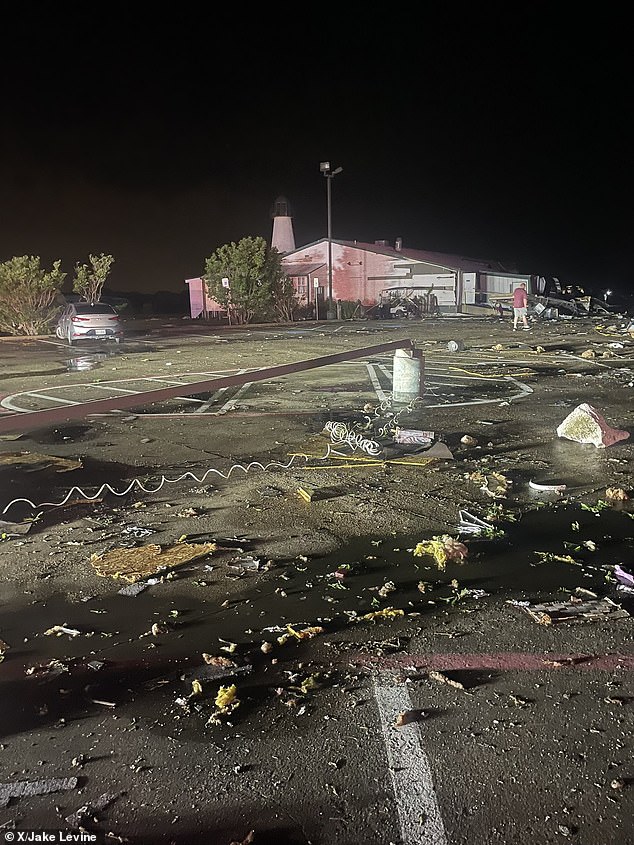 Debris is scattered in this parking lot and a man is seen wandering through the damage early Sunday morning