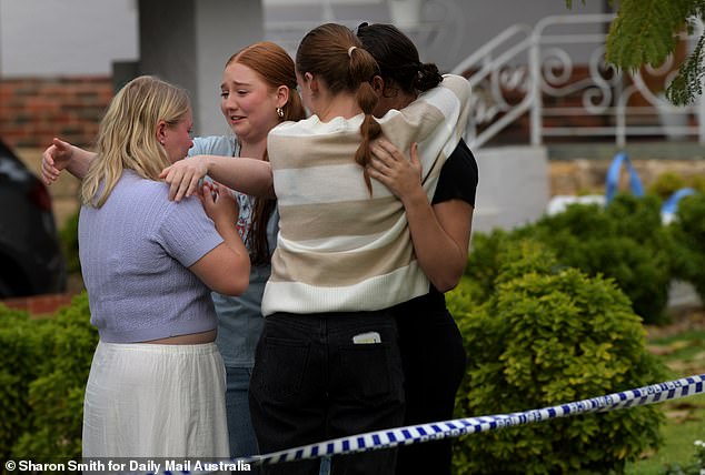 Pictured: Mourners comfort each other after leaving floral tributes outside the murder scene