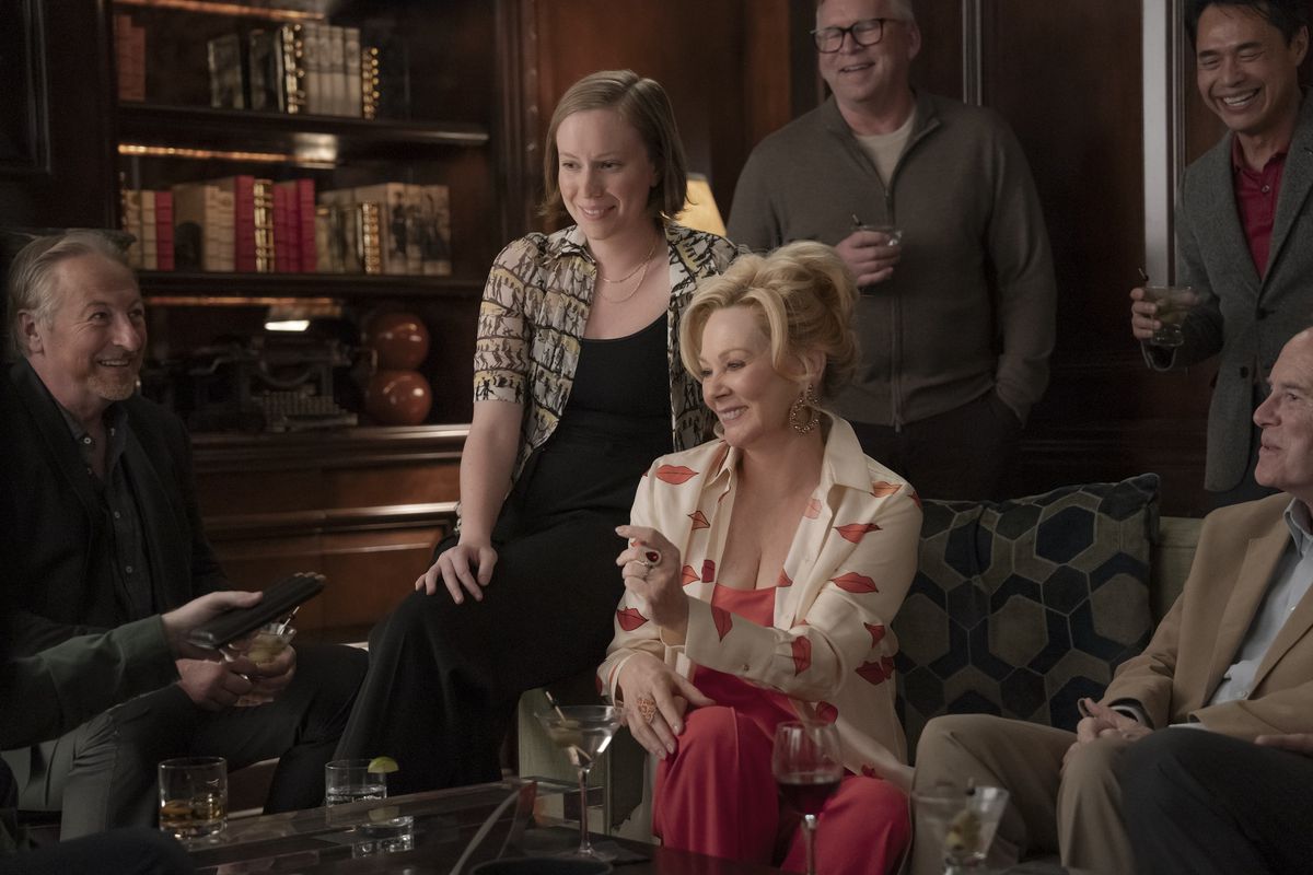 Deborah (Jean Smart) sits smiling with Ava (Hannah Einbinder) on the armrest of her chair in a still from Hacks