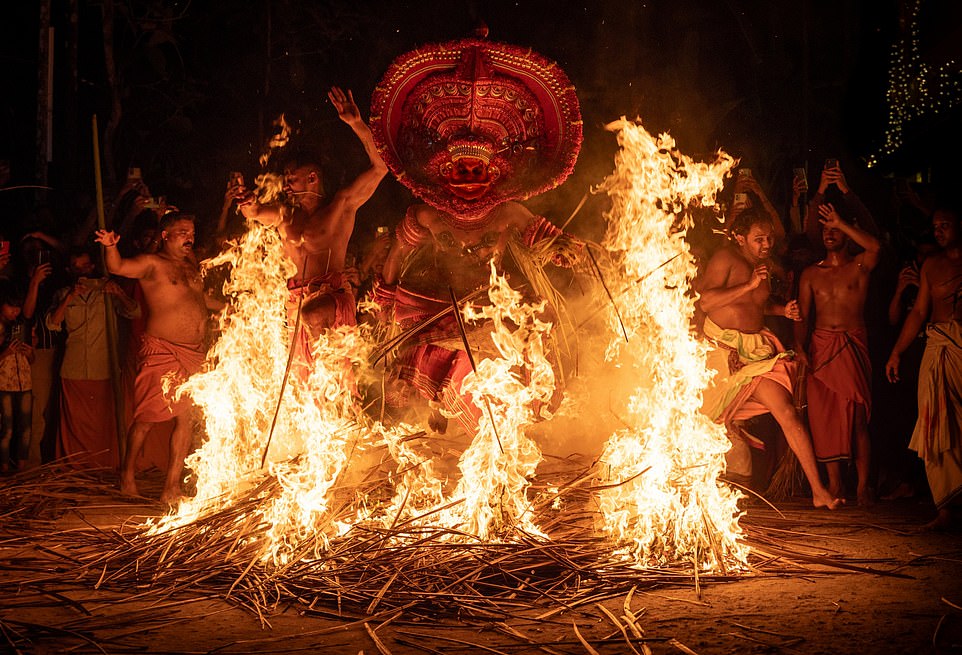 KERALA, INDIA: A man dressed as a deity jumps through a raging fire during a 3am ceremony for the Kandanar Kelan Theyyam – a Hindu religious ceremony