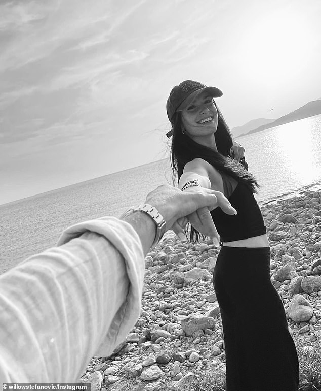 The photo shows Willow holding the outstretched hand of a mystery man and smiling at the camera while standing on a beach