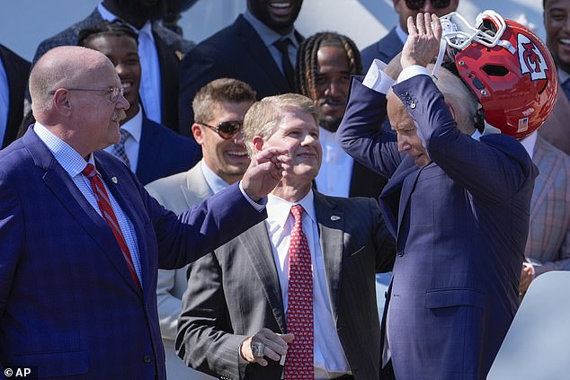 Kansas City Chiefs coach Andy Reid (left) and CEO Clark Hunt (center) help President Joe Biden remove the helmet that was brought to the White House as a gift from the team