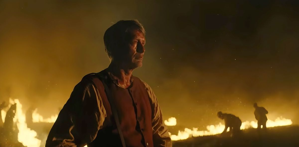 Mads Mikkelsen standing in front of a burning landscape