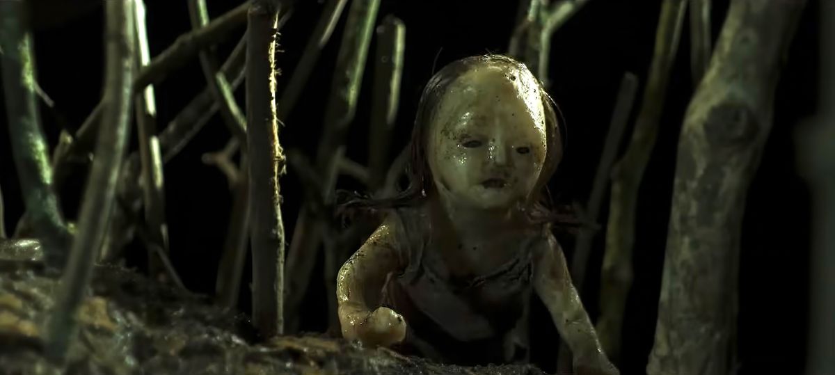 A melted-looking doll crawls in a forest