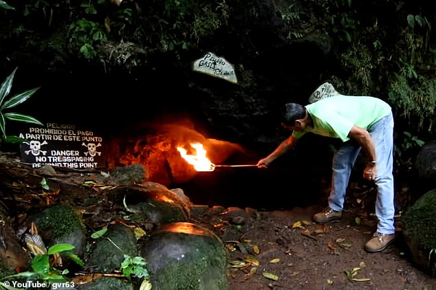 Visitors to the Cave of Death demonstrate its power by holding a lit torch near the entrance.  Note the warning sign, decorated with deadly skulls and crossbones, that reads: 'Danger!  Do not enter from here'