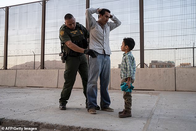 A Guatemalan migrant is searched by a federal immigration officer as his son, 6, watches in El Paso, Texas