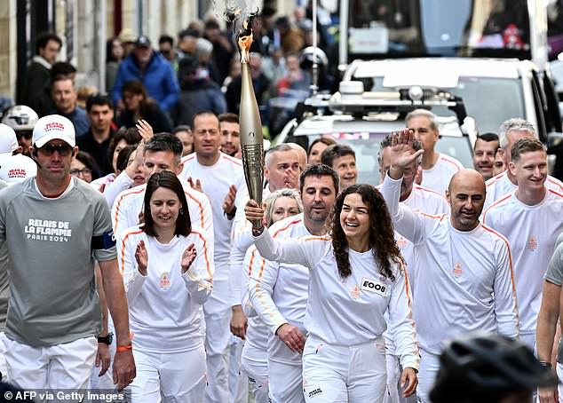 Members of the public watch a torchbearer holding the Olympic torch as part of the Olympic and Paralympic torch relay, ahead of the Paris 2024 Olympic and Paralympic Games, in Saint-Emilion, south-west France, on Thursday, where police foiled a plot to launch a mass attack