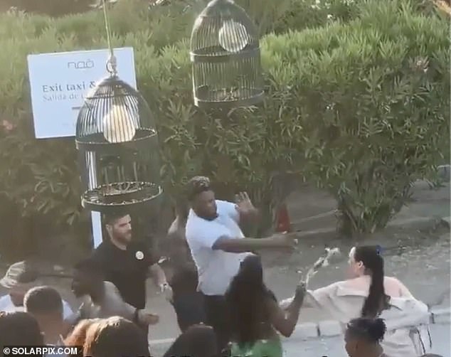 A security guard is seen punching a woman in a green dress who tried to wave her bag at him