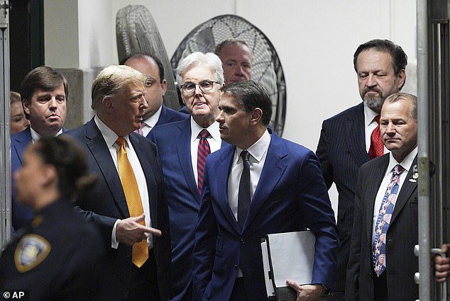 Trump speaks with his lawyer Todd Blanche, surrounded by the rest of his entourage