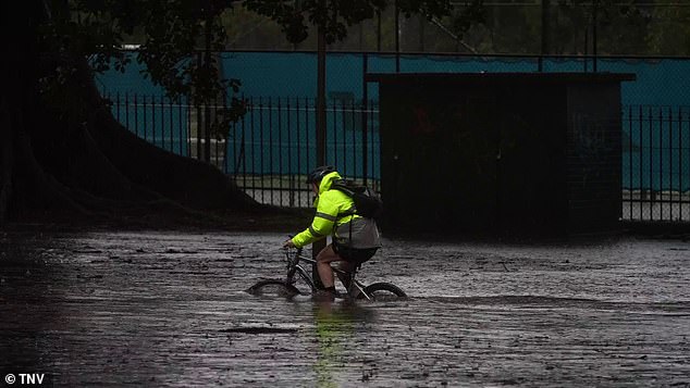 A cyclist is seen riding through flooded roads in Moore Park, in Sydney's east