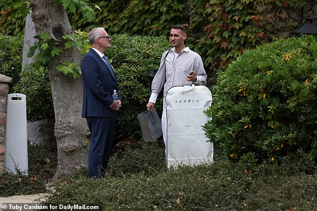 Two men stand outside Moraga talking.  The man on the right appears to be holding a suit