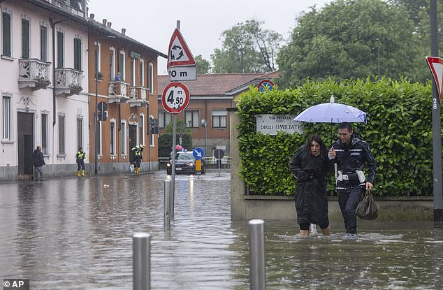 A city police officer helps a woman cross a road after part of the city was flooded following persistent rain in Milan, Italy last month