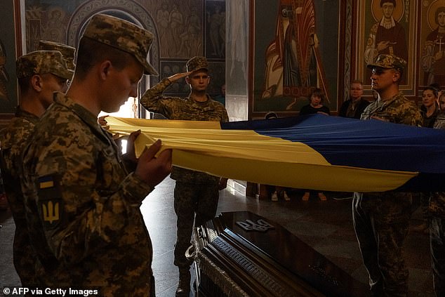 Ukrainian soldiers hold a national flag over the coffin of Ukrainian soldier Ruslan Troianchuk, call sign "Friend"who was murdered in the Donetsk region