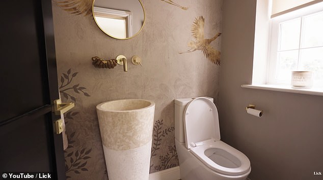 A downstairs toilet contains a cylindrical washbasin with subtle plant motif wallpaper - with the taps and mirror finished in a stylish gold tone