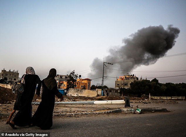 Two Palestinian women walk past the ruins of a building in Al Bureij