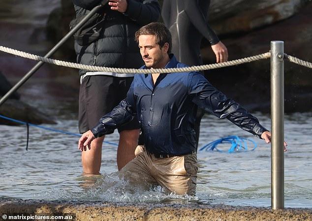 Wearing a blue button-up and khaki pants, the Wolf Creek star was soaked to the bone as he trudged his way out of the depths and onto dry land.