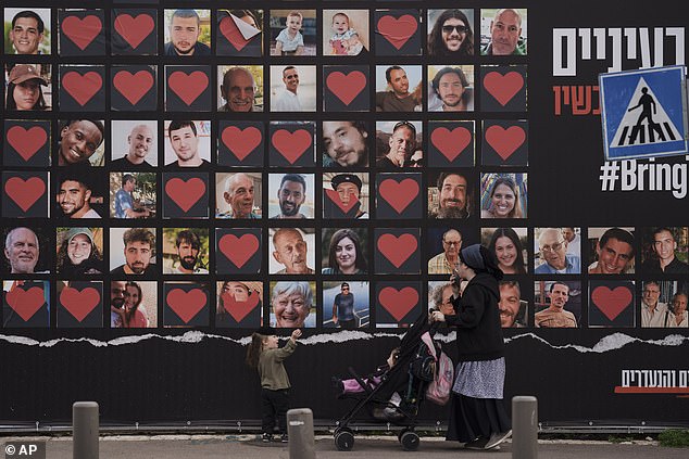 A woman and her children walk past a wall with photos of hostages kidnapped during Hamas' cross-border attack on October 7