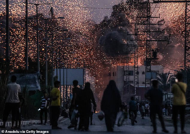 Palestinians stand on a road as black smoke and flames rise over a building following the Israeli attacks in Deir al-Balah, Gaza on June 6