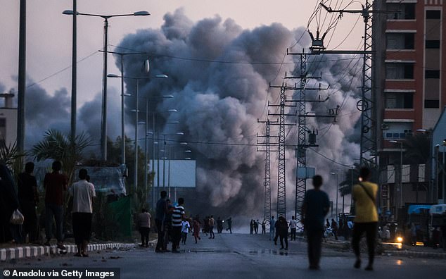 Palestinians stand on a road as black smoke rises over a building following the Israeli attacks in Deir al-Balah, Gaza on June 6