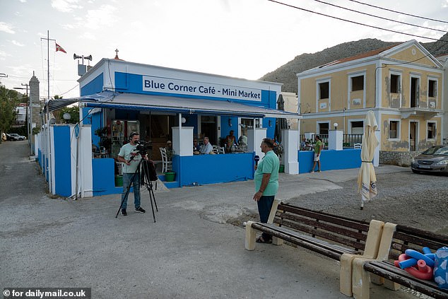 A camera crew can be seen recording in front of the Blue Corner Café in Symi