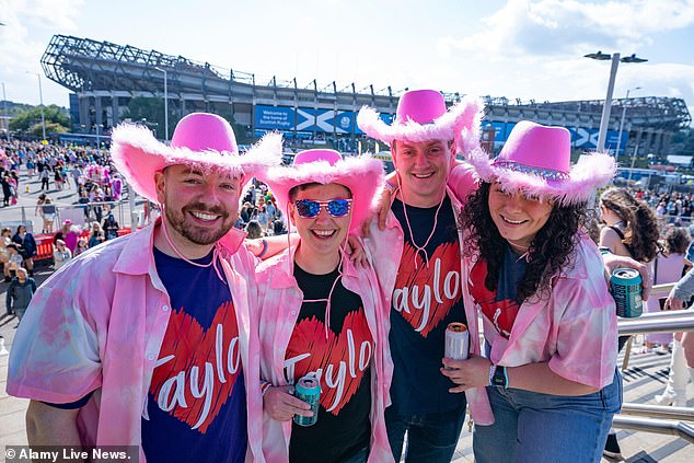 A group of Swifties wearing pink feather cowboy hats and Taylor T-shirts pose outside the stadium