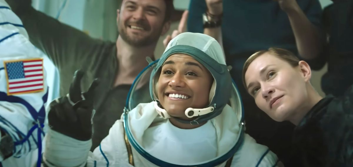 An astronaut poses for a photo with some colleagues.  She holds her fingers in a peace sign.