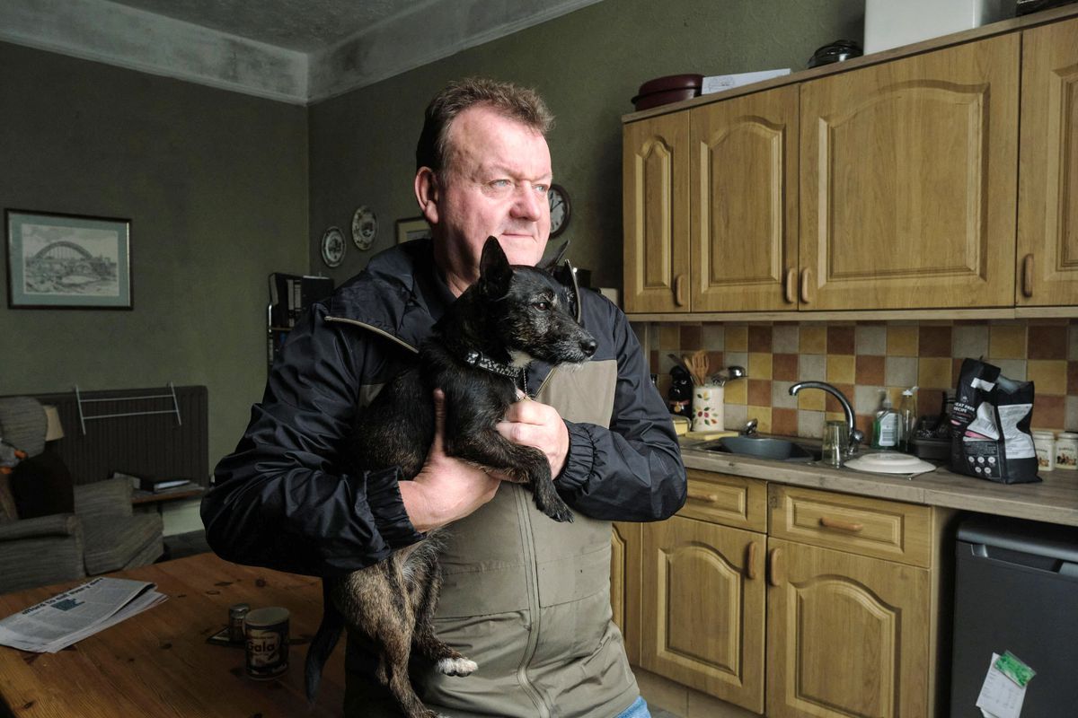 A man holding a small black dog while standing in a kitchen