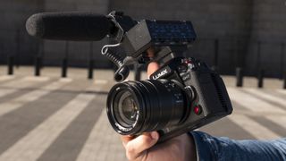 Panasonic Lumix GH7 camera in hand with DMW-XLR2 microphone adapter attached