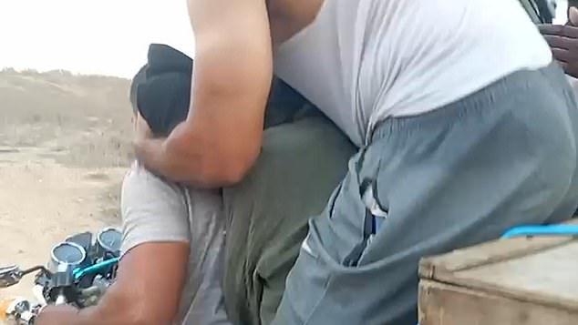 In the footage published in April, the woman can be heard wailing as she is assaulted by a Palestinian fighter, who holds her head down as he places a black bag over her face (pictured)