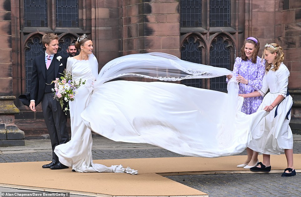 A bridesmaid and the bride's mother struggle to keep Olivia's veil in the wind