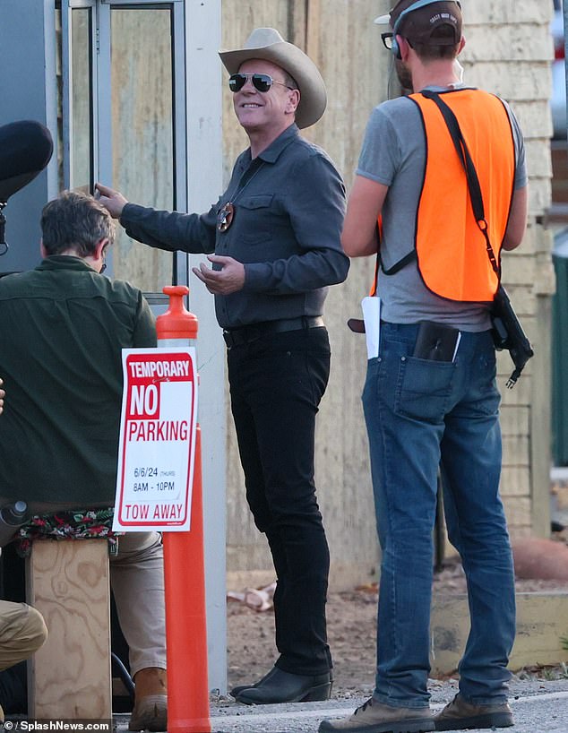 In another scene, the 24 alum was dressed in black jeans and boots, with a gray button-up shirt with the hat and badge, and entered a phone booth.