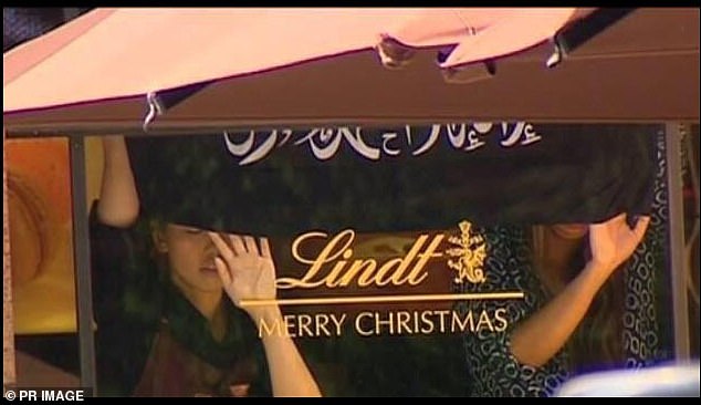 Hostages are pictured holding up a black flag with Islamic script at the Lindt Café in December 2014