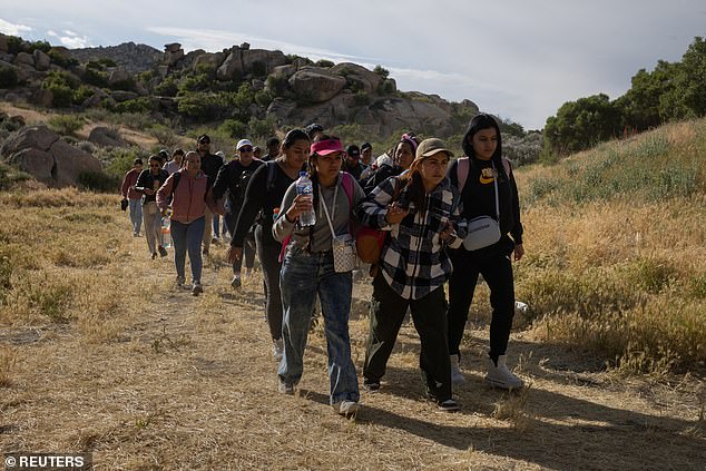 SEI*207607621 Migrants from South and Central America hold hands as they walk toward a hole in the border wall before crossing Boulevard, California