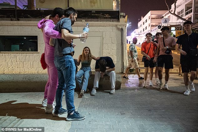 Police officers struggled to cope as the young, drunk revelers appeared worse for wear as some passed out on the sun loungers while others were carried home by their friends in the early hours of the morning.  A woman is seen with two men, with their heads on their knees, on a street in Magaluf