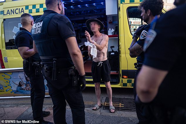 The man in the hat protests alongside police officers next to an ambulance in Magaluf