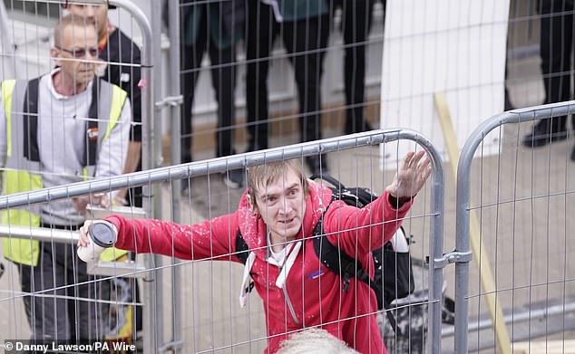 The man holds a coffee cup in his left hand as workmen look on before rushing to grab him